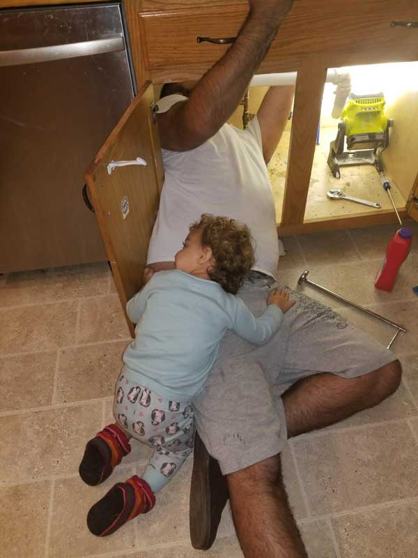 My daughter laying on top of my while working under the kitchen sink.